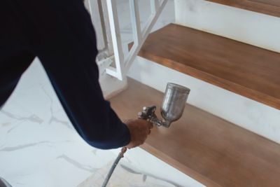 A construction worker applies varnish on the stairs. Using an airbrush for the application. Renovation or finishing works.