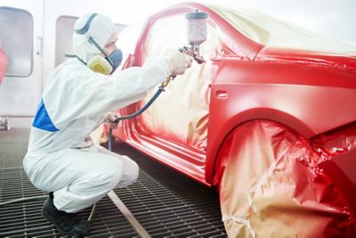 auto mechanic worker painting a red car in a paint chamber during repair work