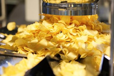 A conveyor belt is covered with potato chips as part of the snack packaging process