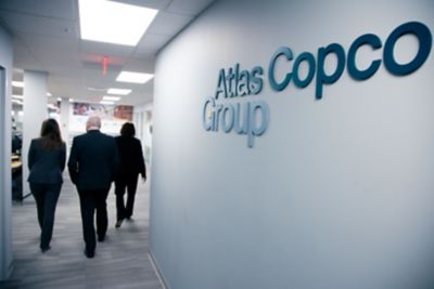 Medarbetare går med ryggen mot kameran i en kontorskorridor med Atlas Copco Group-loggan i förgrunden.