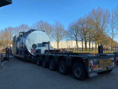 A 22-ton boiler on a special convoy truck leaving Eco Steam and Heating's' depot. Trees and a clear blue sky are in the background.