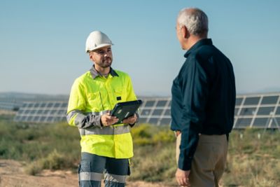 Technician and executive in conversation in front of field of solar panels