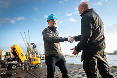 Atlas Copco estrechando la mano a un cliente en una obra en construcción con compresores portátiles de alquiler