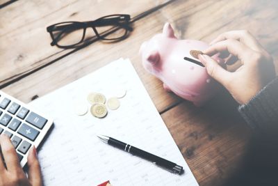 Female hand putting coin in piggy bank, on the office desk