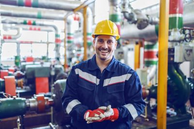 Handsome smiling caucasian hardworking blue collar worker in protective suit and with hardhat on head standing in factory.