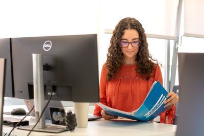 Araceli tras su escritorio de oficina abriendo una carpeta de Atlas Copco sobre su mesa elevable