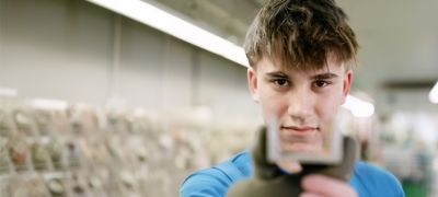 Junger Mann mit kurzem Haar blickt konzentriert durch ein Werkstück in der Atlas Copco Energas Werkstatt 