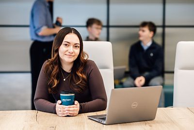 A female apprentice sitting in a meeting room with a laptop looking at the camera
