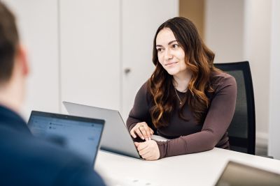 A young professional woman employee engaged in a discussion at an office desk with colleagues, emphasizing teamwork, collaboration, and productive communication.