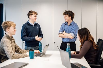 A group of students chatting whilst working on laptops