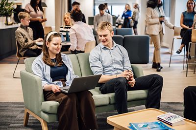 Employees sitting on sofas working on a laptop whilst chatting