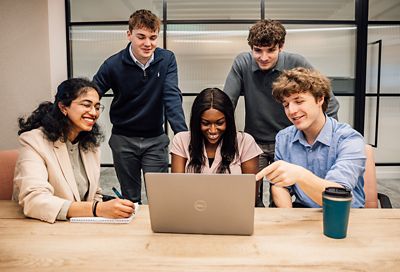 A group of employees looking at a laptop smiling whilst working together