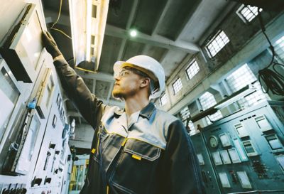 Industrial technician using a tablet to inspect piping and valve systems in a complex industrial installation.