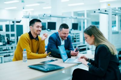 Employees sitting at a desk and working together on the factory floor 