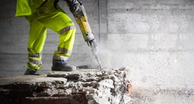 Construction worker using heavy-duty jackhammer tool and breaking reinforced concrete banner