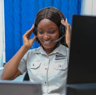 A Picture of an Atlas Copco female employee happily attending to a virtual client while wearing headphones.