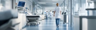 A healthcare professional in a white coat walking through a hospital corridor.