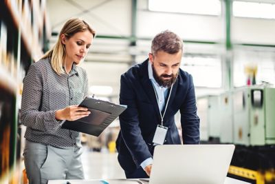 A portrait of a serious mature industrial man and woman engineer with laptop in a factory, working.