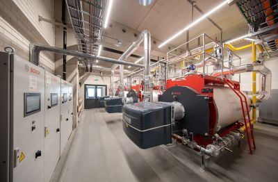 Industrieraum mit mehreren großen Heißwasserboilern der Marke Bosch, verbunden mit Edelstahlrohren und elektronischen Schaltschränken