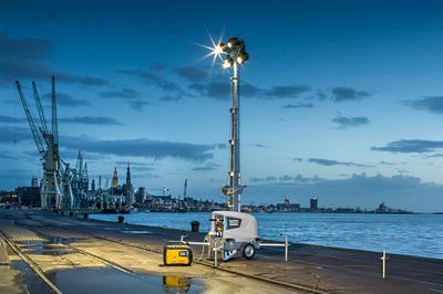 Atlas copco's electric-powered mobile light tower providing bright site lighting near an industrial waterfront location.