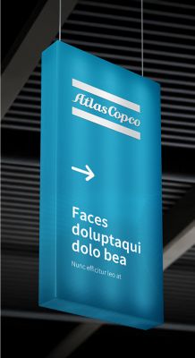 A rectangular sign in blue with a white Atlas Copco logo and some text hanging from the ceiling