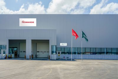 Facade of a facility showing logotype of only Edwards. Edwards and the Group flags are in front, and a Group logo sign with a white background.