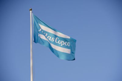 A blue Atlas Copco flag with the sky in the background