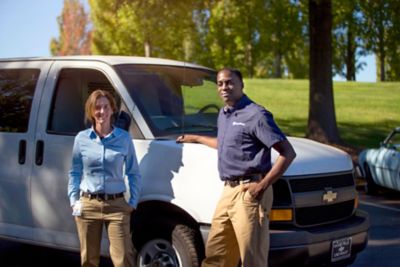 Male and female service techs stand in front of white van