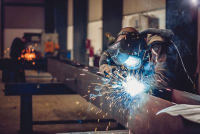 Industrial Welder With Torch and Protective Helmet in big hall welding metal profiles
