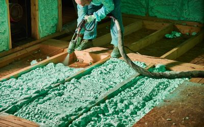 Male builder insulating wooden frame house. Cropped view of man worker spraying polyurethane foam on floor inside of future cottage, using plural component gun. Construction and insulation concept.