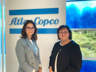 deux femmes posent devant un logo Atlas Copco bleu