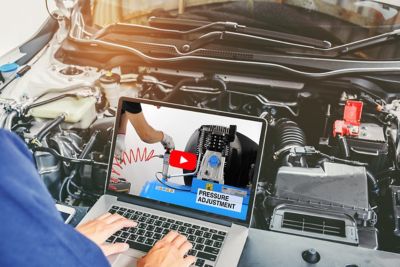Professional car mechanic working in auto repair service using laptop bon car, watching an air compressor maintenance video