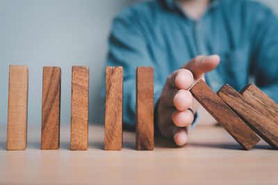 Wooden bricks standing on a table, a hand is stopping them from falling. 