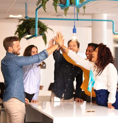 Five Atlas Copco employees standing around a desk and high-fiving 