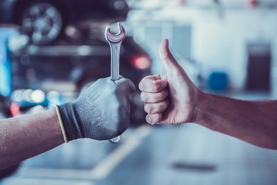 Cropped image of mechanics working in auto service. One is holding a spanner while the other is showing Ok sign