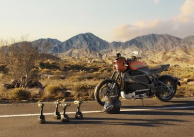 3D Generated image of a motorcycle standing on a road with mountains in the background.  in the foreground of the image there are 4 Atlas Copco tools standing.