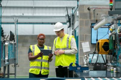 An apprentice being shown something on an ipad in a manufacturing facility