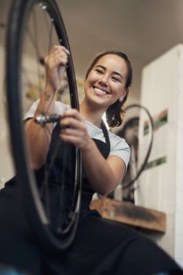 Foto di una giovane donna in piedi da sola nella sua officina che ripara una ruota di bicicletta