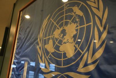 The United Nations logo in gold on a glass wall.