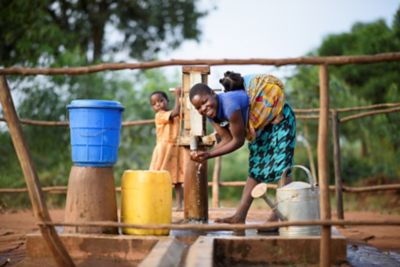 Kvinna med barn pumpar vatten i Malawi