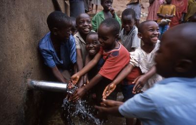 Happy African children by water tap with pouring water.