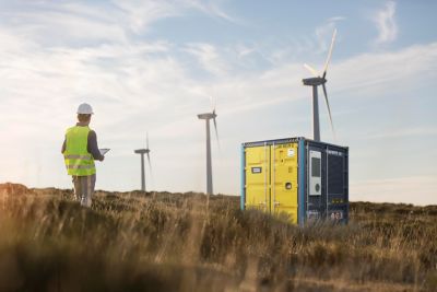 A man wearing a reflective jacket stands at a wind farm, looking at wind turbines powered by generators.