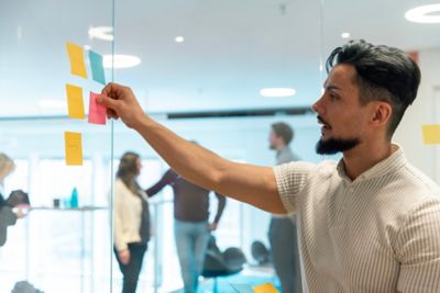 An employee observing and sticking notes onto a board with colleagues nearby. 