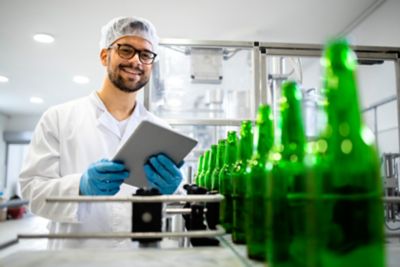 Alcohol drinks or beverage industrial production and factory worker controlling quality of glass beer bottles.