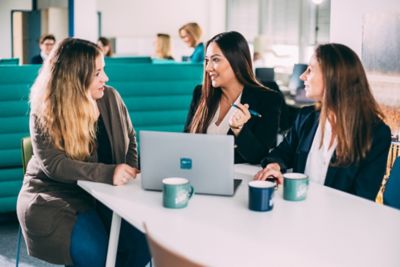 Three women engage in a discussion in office using a laptop. The image illustrates collaboration and teamwork in a modern workspace setting, reflecting productivity and mutual communication.