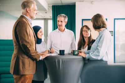 A group of business professionals from diverse backgrounds interacting positively in an office setting, showcasing teamwork and collaboration.
