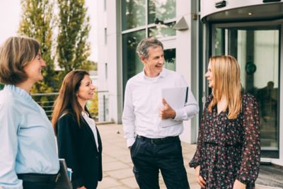 A group of professionals stands outside a modern office, smiling and interacting positively.