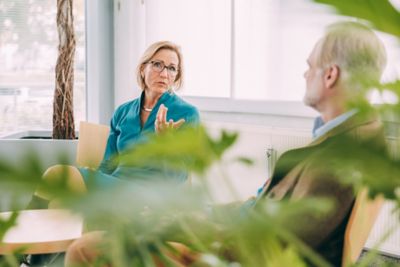 Two employees deeply engaged in conversation, suggesting collaboration, discussion, or mentoring. The modern setting and foliage highlight a productive and professional atmosphere.