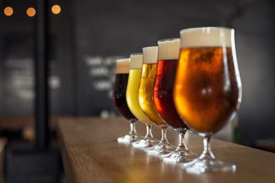 Image of glasses with different sorts of craft beer on wooden bar. Tap beer in pint glasses arranged in a row. Closeup of five glasses of different types of draught beer in a pub.