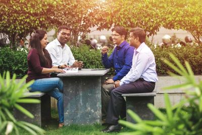 Four colleagues in India sitting at a table outside the office with greenery around. 